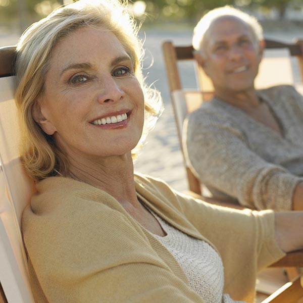 an older white couple lounge on beach chairs with smiles