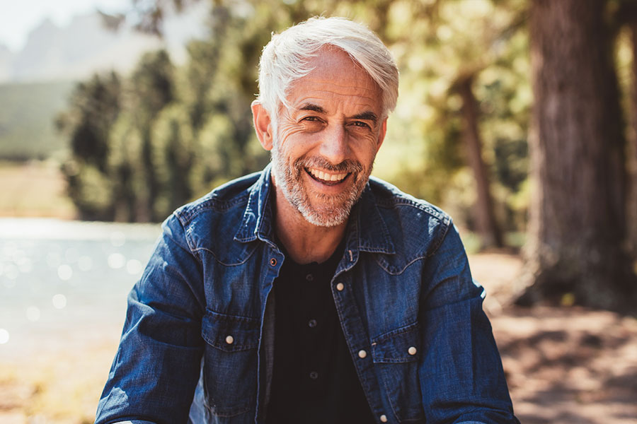 older white man with a bright smile sits outdoors