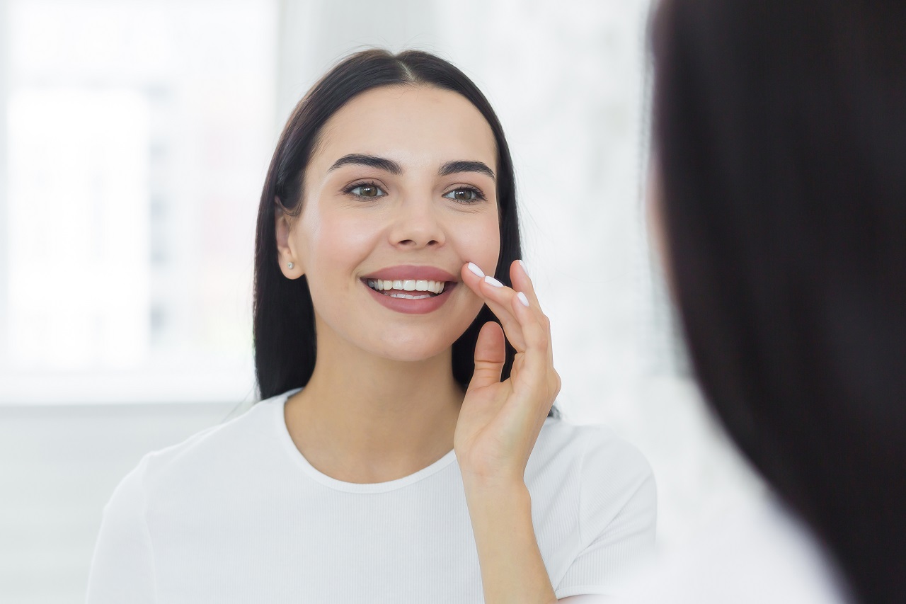 young woman looks in the mirror and smiles examining her teeth