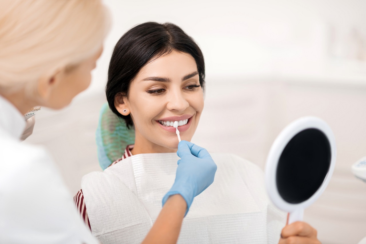 Smiling woman trying on teeth whitening sample looking in the small mirror at dentists