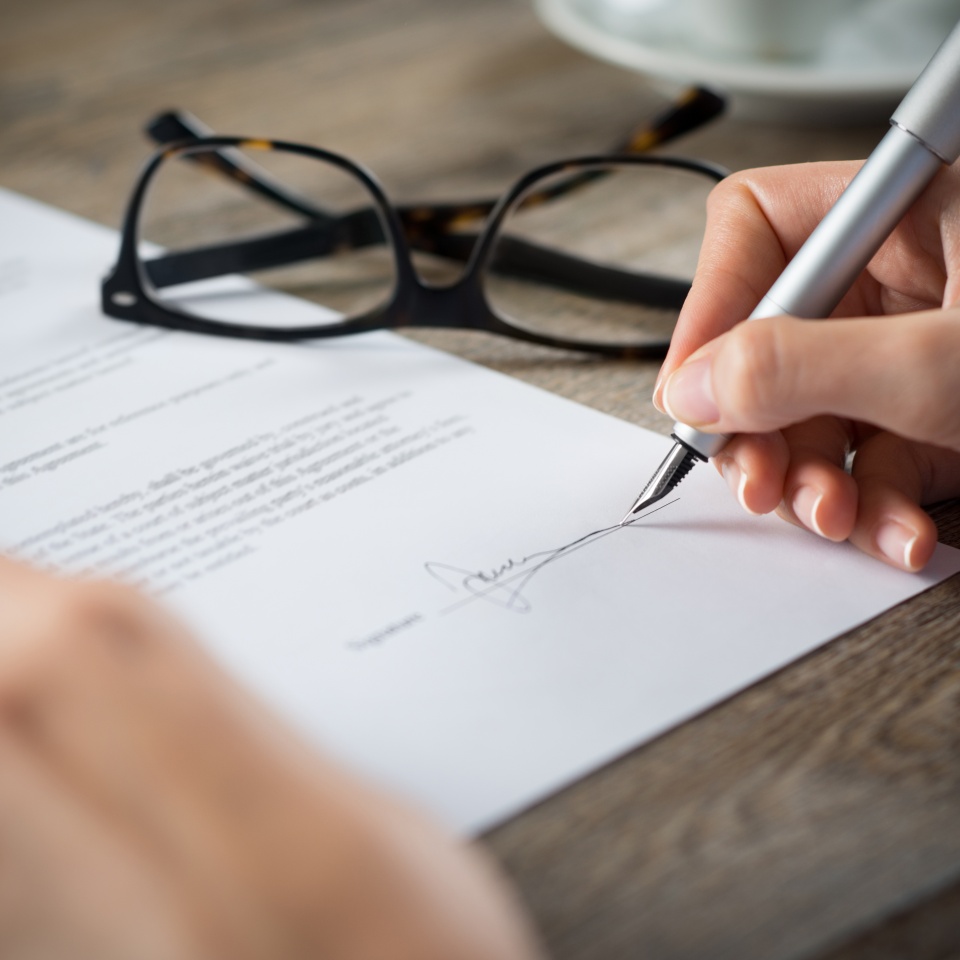 Closeup shot of a woman signing a form. She's writing on a financial contract. Shallow depth of field with focus on tip of the pen.