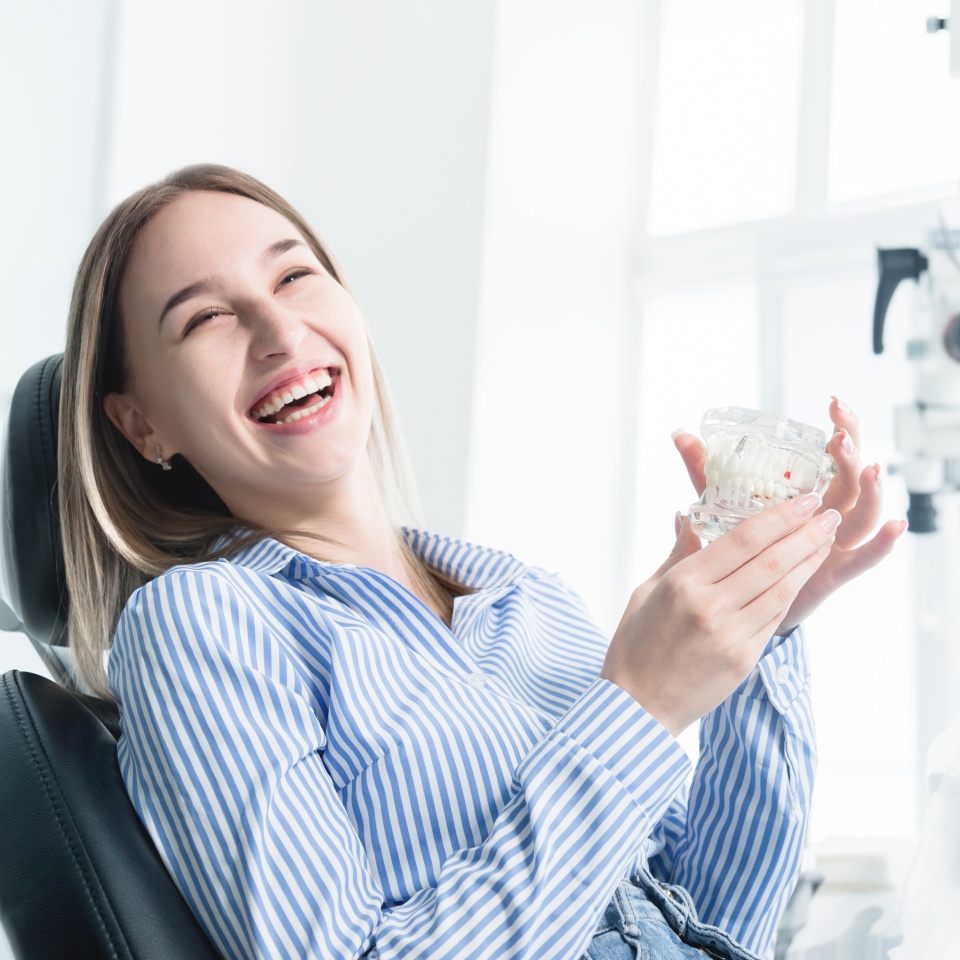 Portrait of a happy attractive girl in a dental chair. Laughing girl at the dentist's appointment with a jaw model in her hands