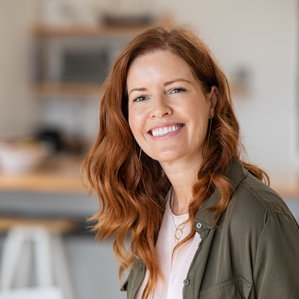 Portrait of smiling mature woman looking at camera with big grin. Successful middle aged woman at home smiling. Beautiful mid adult lady with long red hair enjoying whitening teeth treatment.