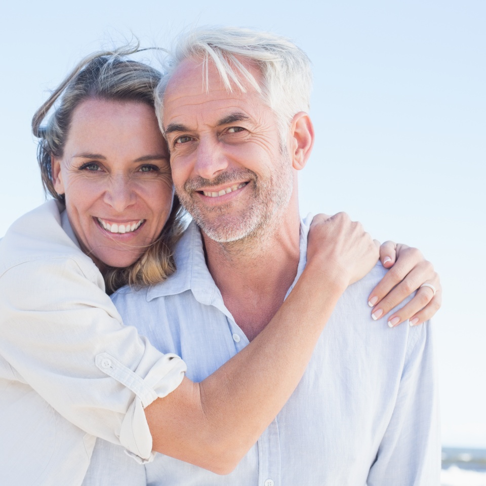 Attractive couple hugging at the beach smiling at camera on a sunny day