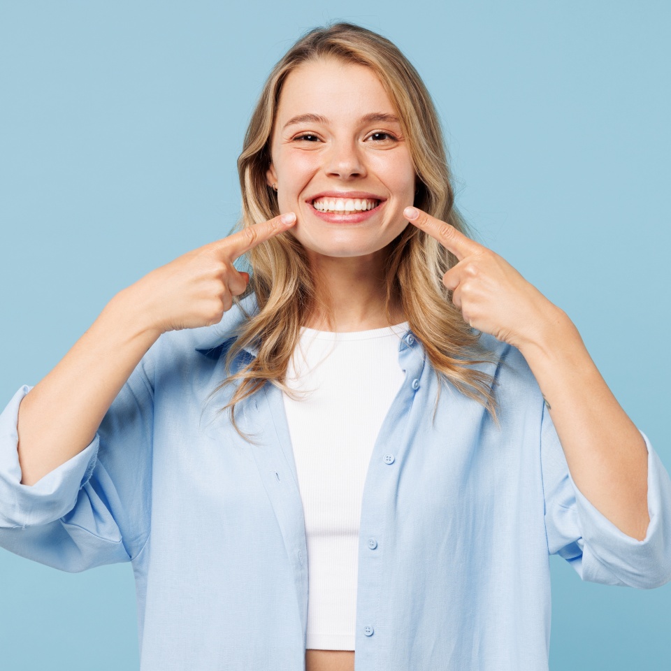 Young smiling satisfied happy woman she wearing white top shirt casual clothes point index fingers on opened mouth teeth isolated on plain pastel light blue cyan background studio. Lifestyle concept