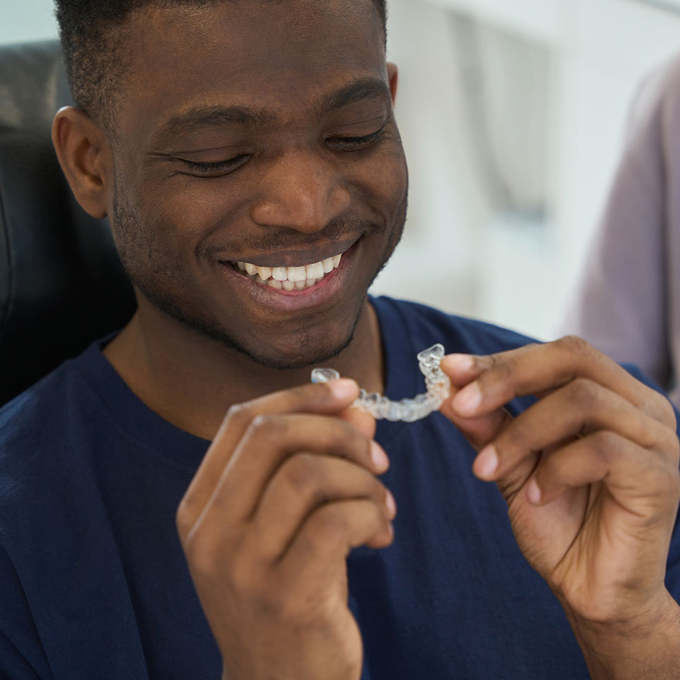A man in a navy blue shirt smiles while holding a clear dental aligner with both hands.