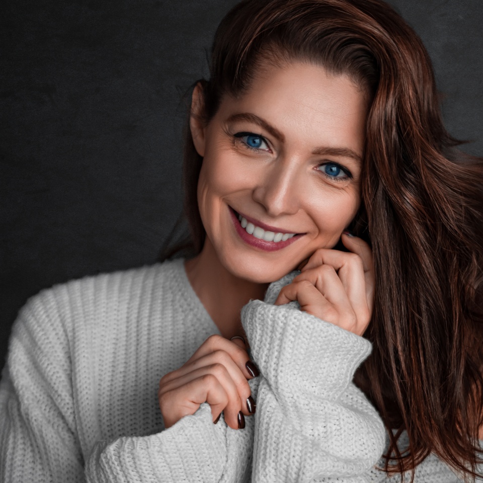 Smiling blue eyed 40 years old woman looking at camera. Photo over dark grey background. Psychology and feminine health concept.