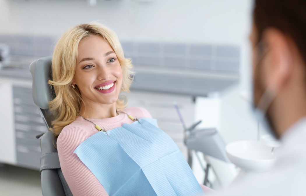 Relaxed blonde woman smiling to her dentist, side view, copy space. Peaceful pretty young lady having conversation with her doctor stomatologist, enjoying modern treatment at new dental clinic