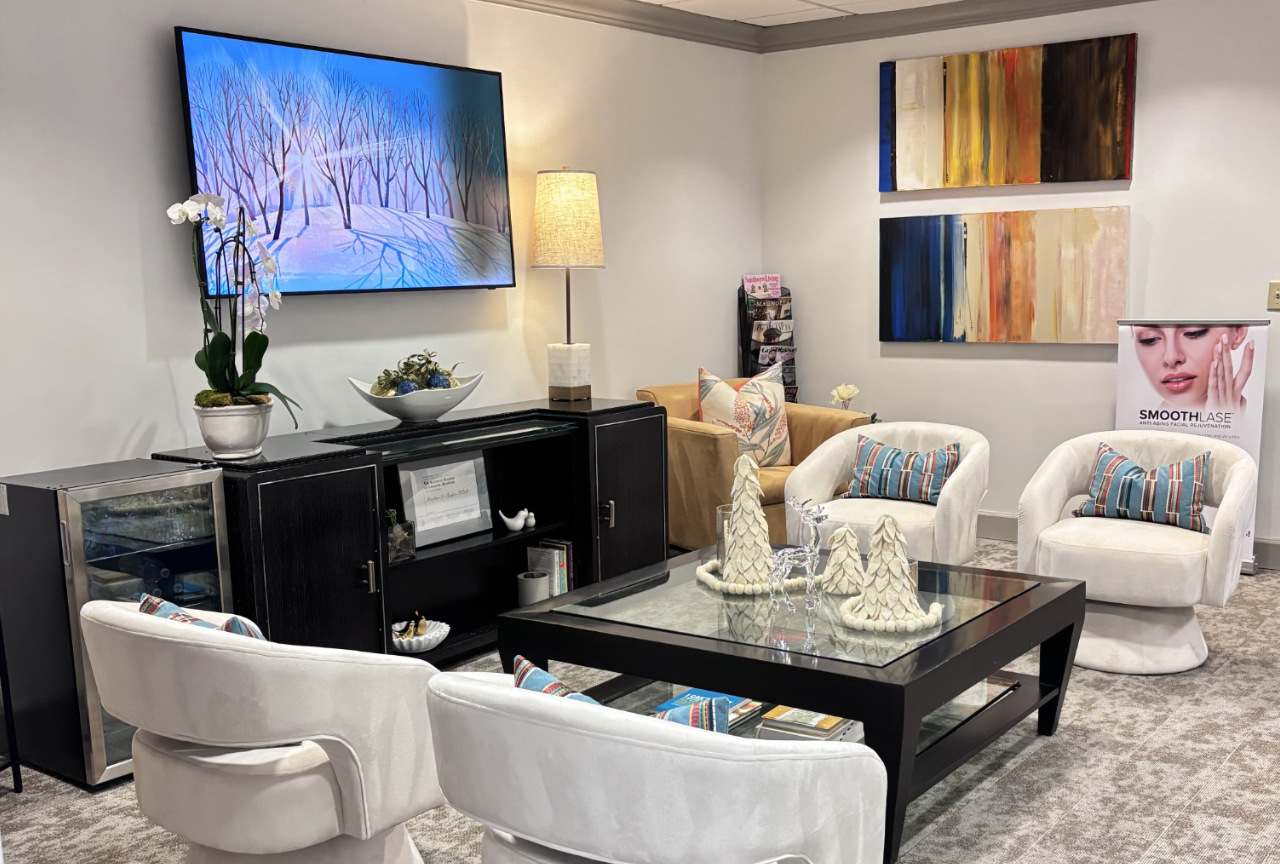Waiting area with a television, a dark wood cabinet, armchairs, a coffee table with decorative trees, and a sign for Smoothlase skin rejuvenation.