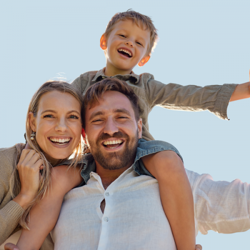 a mother and father stand side by side with a young boy on his father's shoulders